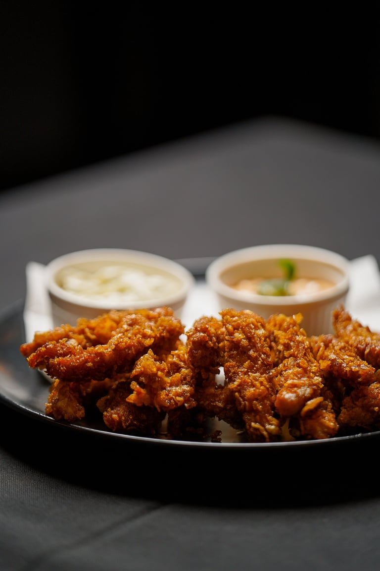 Crispy fried chicken pieces on a black plate with two white bowls of dipping sauces in the background