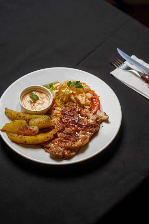 Grilled meat with crispy potatoes, caramelized onions, and creamy sauce on a white plate