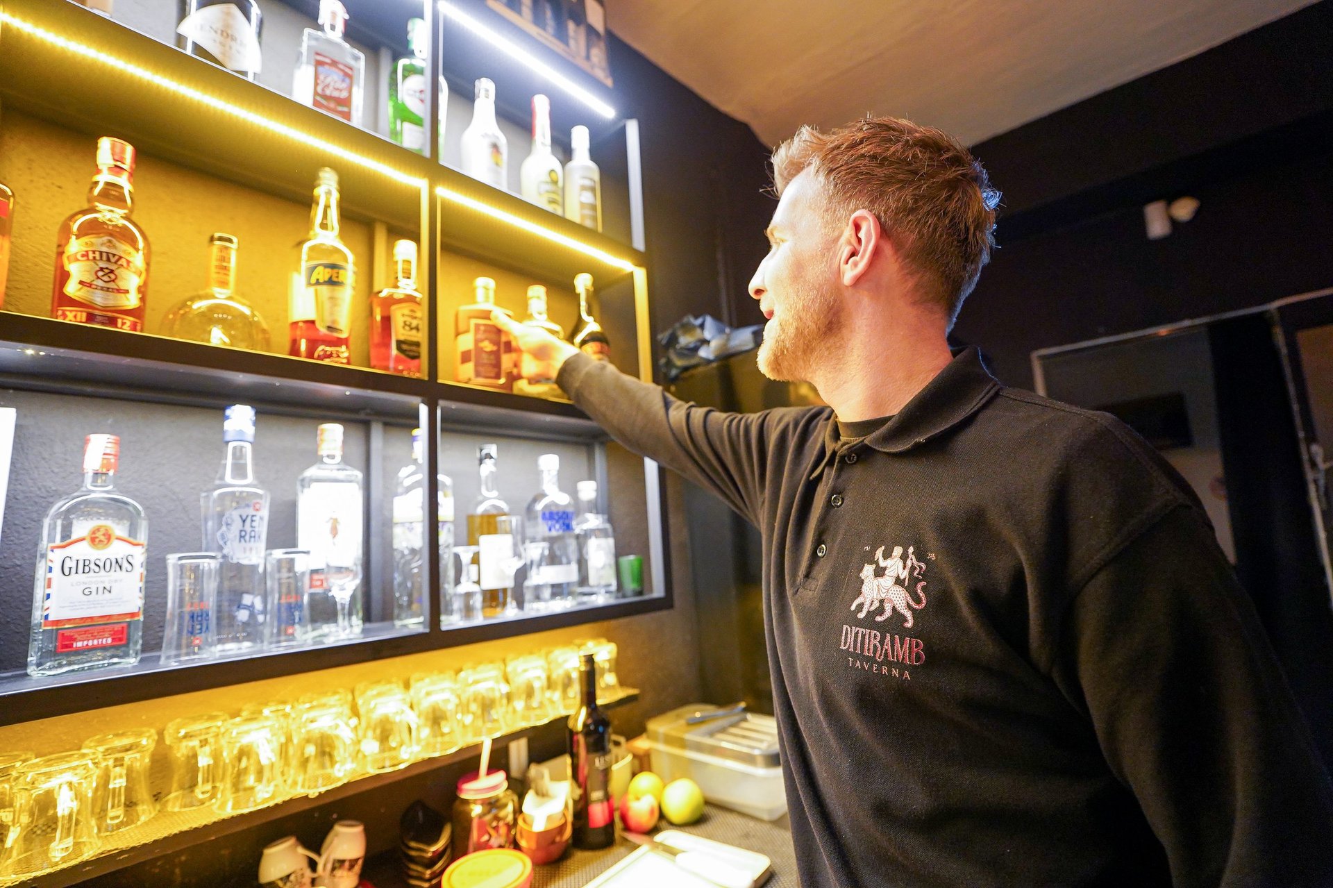 Man reaching toward illuminated shelves displaying bottles of whiskey and spirits in a bar