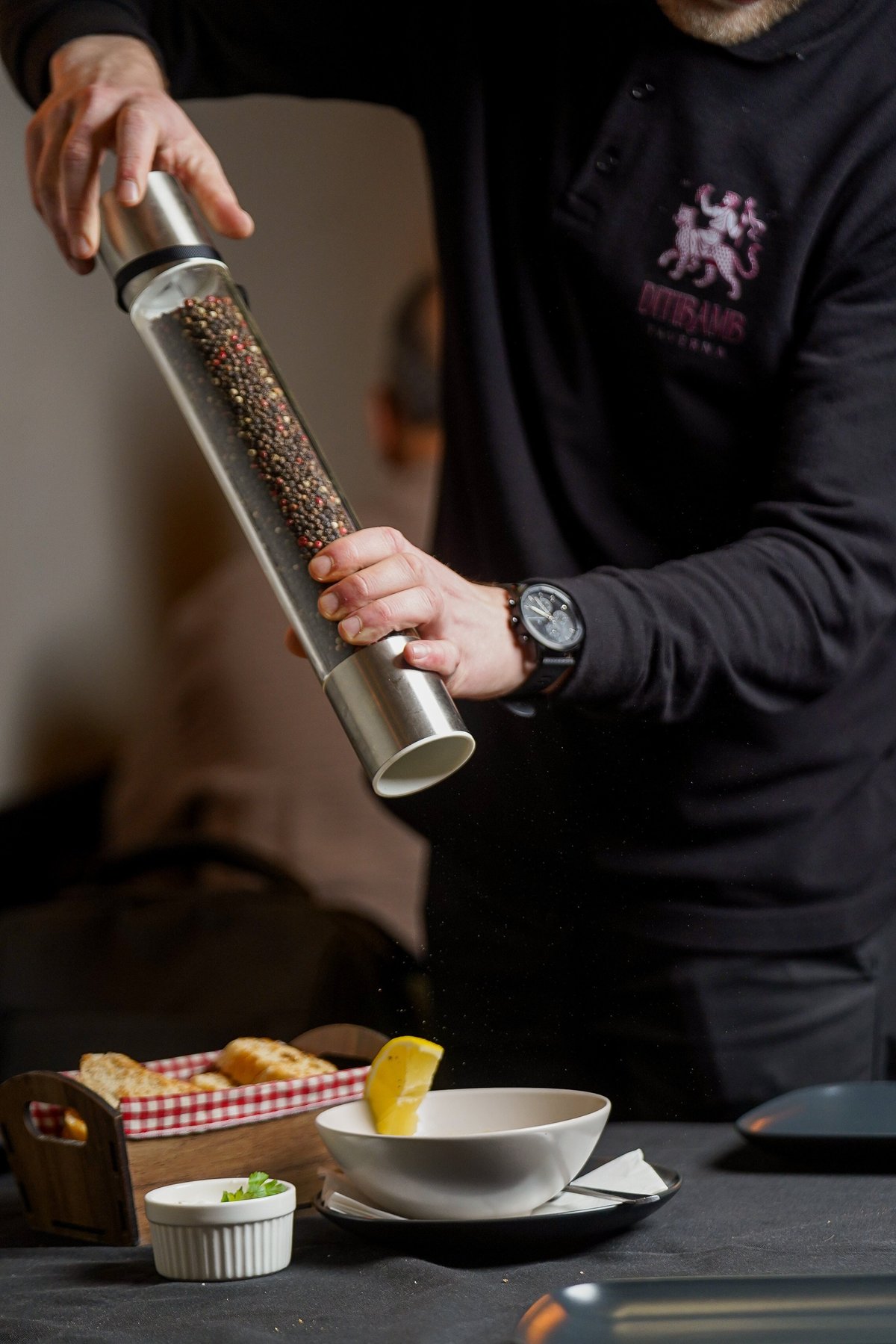 Chef in black uniform grinding pepper from a mill over a white bowl at a plated food service station