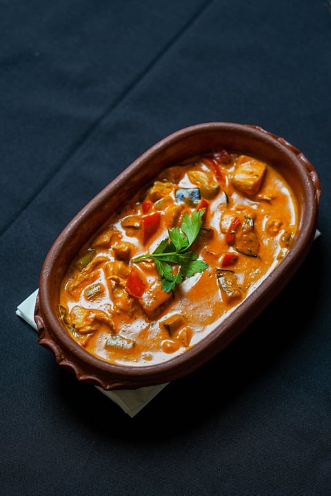 Creamy curry dish with chicken or meat chunks in a terracotta bowl garnished with fresh basil on dark slate background